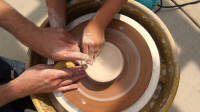 Two sets of hands making a pot on a pottery wheel